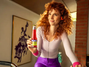 Negroni mocktail bottle held by a smiling person wearing retro workout clothes indoors