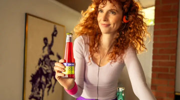 Negroni mocktail bottle held by a smiling person wearing retro workout clothes indoors