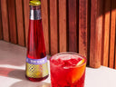Negroni mocktail served on ice with an orange twist beside a Phony Negroni bottle on a sunlit surface
