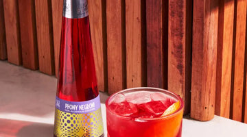 Negroni mocktail served on ice with an orange twist beside a Phony Negroni bottle on a sunlit surface