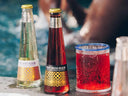 Alcohol-free cocktail bottles beside a fizzy red drink by the pool