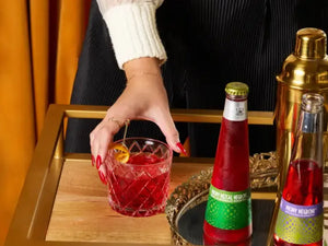 Alcohol free Negroni in a rocks glass being picked up beside Phony Mezcal and Phony Negroni bottles on a bar cart