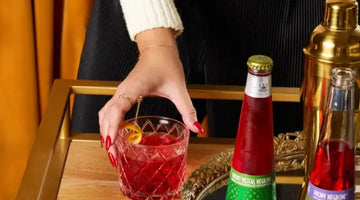 Alcohol free Negroni in a rocks glass being picked up beside Phony Mezcal and Phony Negroni bottles on a bar cart