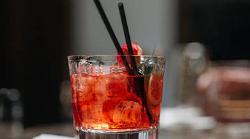 Holiday Negroni cocktail with ice, citrus slice, and black straws served in a glass on a napkin