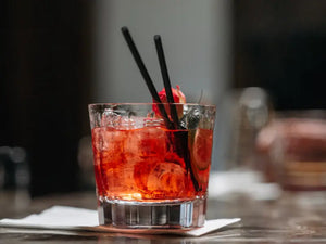 Holiday Negroni cocktail with ice, citrus slice, and black straws served in a glass on a napkin