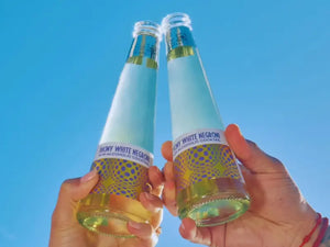 Non-alcoholic Negroni bottles held up against a clear blue sky in a celebratory toast