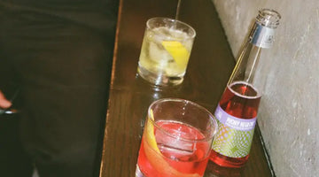 Phony Negroni served in a glass with citrus garnish beside its bottle on a dark bar surface