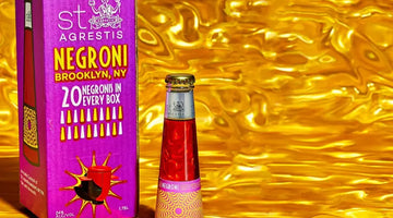 Top Negroni mocktail bottle displayed beside a vibrant purple box against a shiny gold background
