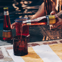 Espresso negroni being poured from a bottle into a glass beside a pool, with another filled glass and bottled drink in the background.