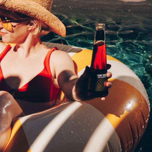 Non alcoholic negroni bottle held by a woman lounging on a pool float in the sun.