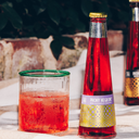 Non-alcoholic negroni in a glass with ice beside a bottled Phony Negroni cocktail on an outdoor table.