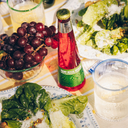 Virgin mezcal negroni bottle on a picnic table with fresh grapes, romaine lettuce salad, and sparkling water.