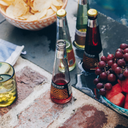 Non alcoholic negroni bottle on a poolside ledge surrounded by fresh grapes, watermelon, potato chips, and other bottled drinks.
